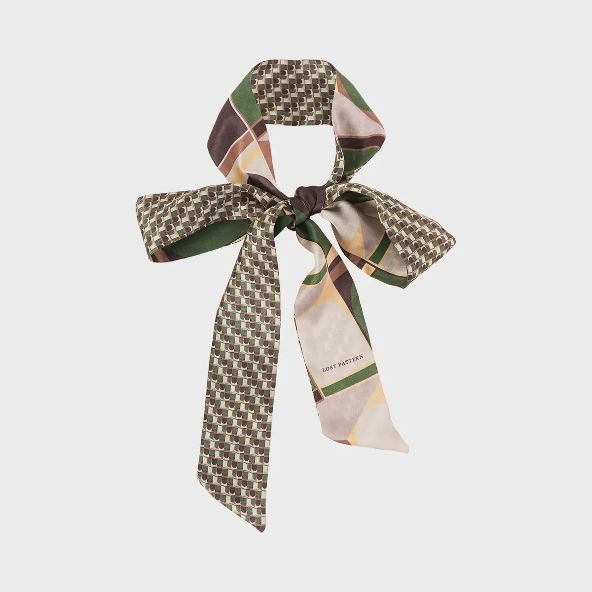 The Modular Silk Skinny Scarf Green by Faire, featuring sophisticated patterns in green, brown, cream, and yellow, is elegantly tied in a high fashion bow shape with long tails.