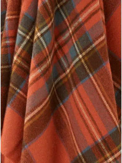 A close-up of Faire's BM Merino Lamb Throw/Blanket reveals its soft Merino lambswool texture, featuring orange, blue, yellow, and brown plaid with diagonal folds and classic clan checkered lines.