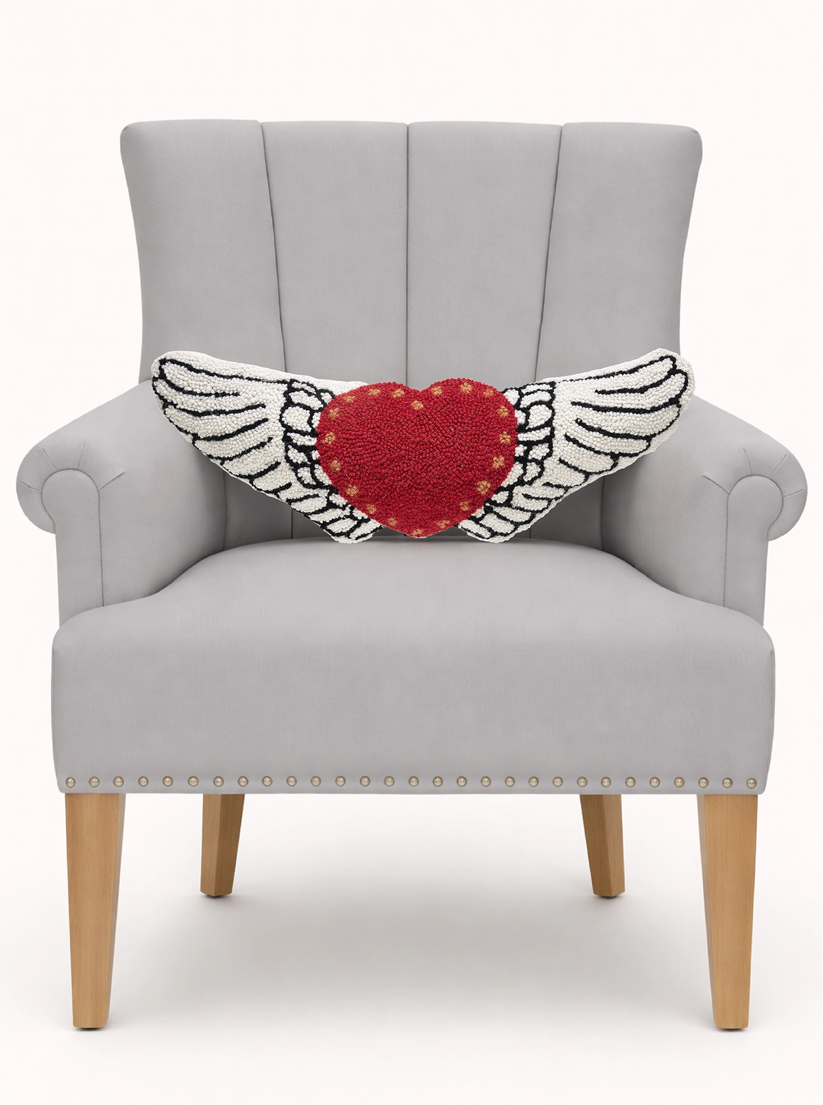 Gray armchair with wooden legs, featuring a red heart-shaped Faire Wing And Hearts Hook Pillow with wings.