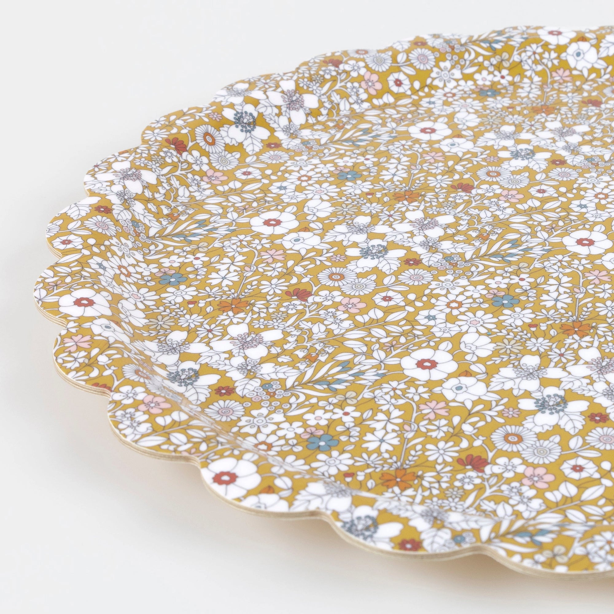 The Meri Meri x Liberty June's Meadow Small Tray by Faire features a decorative scalloped edge and detailed floral pattern in white, gold, blue, and red on mustard yellow, photographed against a plain white background.