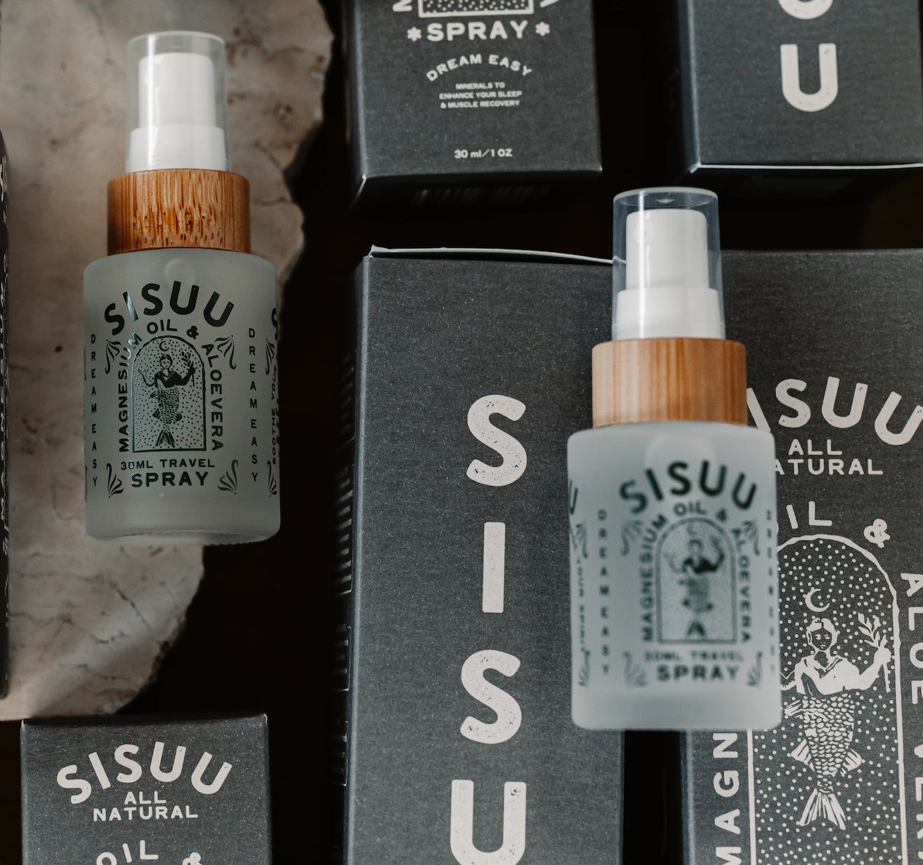 A flat lay displays Faire SISUU Magnesium Oil & Aloe Vera Spray bottles with wooden lids, minimalist labels, and black packaging, highlighting Pure Magnesium Chloride on a neutral surface.