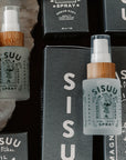 A flat lay displays Faire SISUU Magnesium Oil & Aloe Vera Spray bottles with wooden lids, minimalist labels, and black packaging, highlighting Pure Magnesium Chloride on a neutral surface.