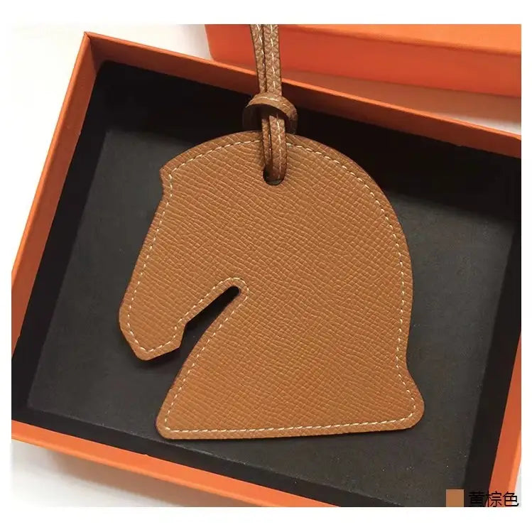 The Faire Bag Charm, a brown leather horse head accessory, comes in an orange and black gift box—perfect for adding a unique, personal touch to your handbag.