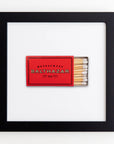 A framed display featuring a red matchbook from Restaurant Balthazar, with matches on the right side, against a white background within an Art Square Black Frame from Match South.