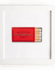 A framed display featuring a red matchbook from Restaurant Balthazar with Arizona style, alongside a row of matches, all against an Art Square White Frame background by Match South.