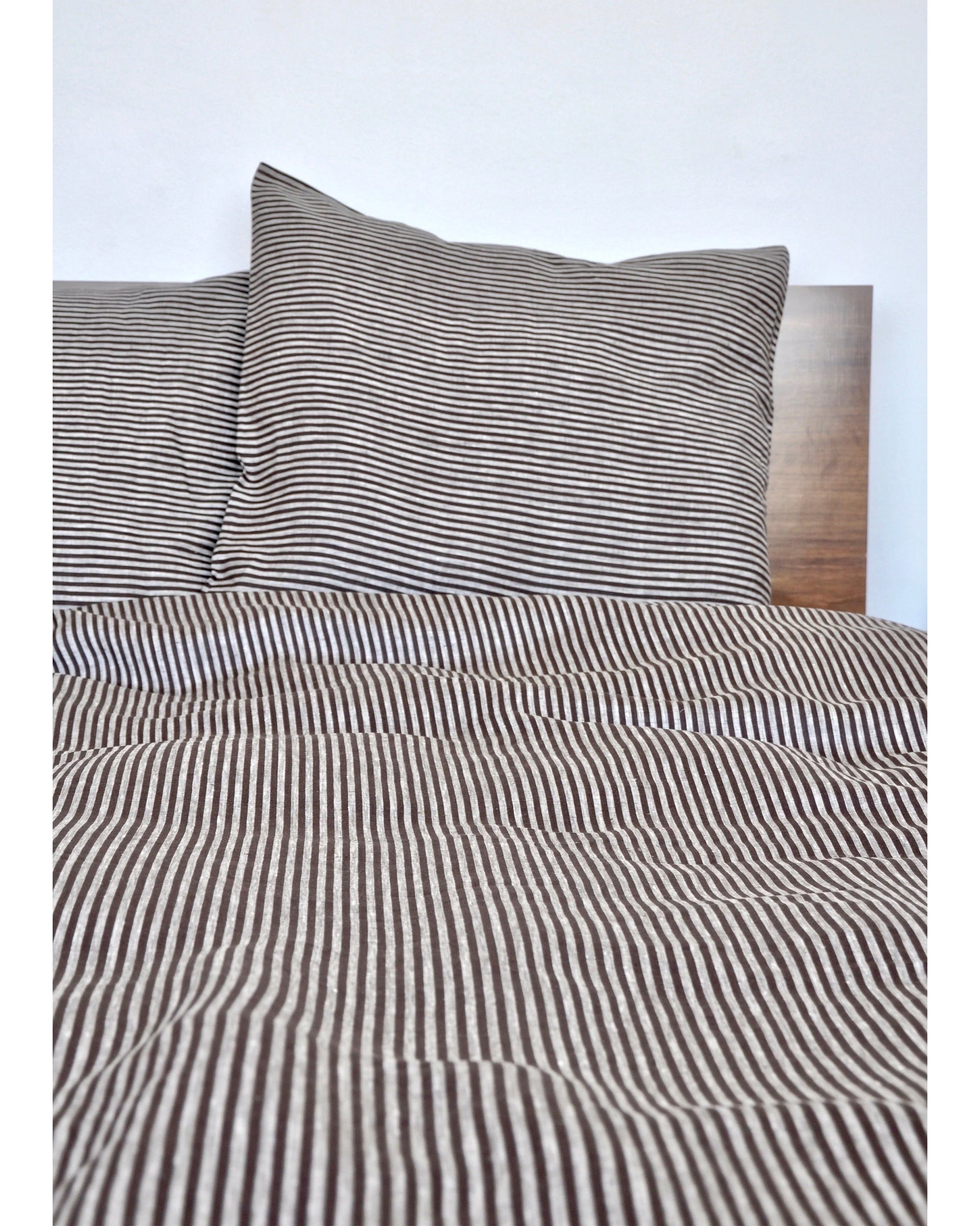 A neatly made bed displays the Modernplum Baltic Queen Duvet in brown and white thin stripes with an invisible zipper, plus a matching pillowcase, set against a wooden headboard and plain white wall.