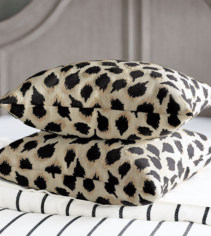 Two PARK AVE ANIMAL chenille pillows by Eastern Accents, featuring a beige and black leopard print, are stacked on a bed with white and black striped bedding, adding a chic animal print accent to the room.