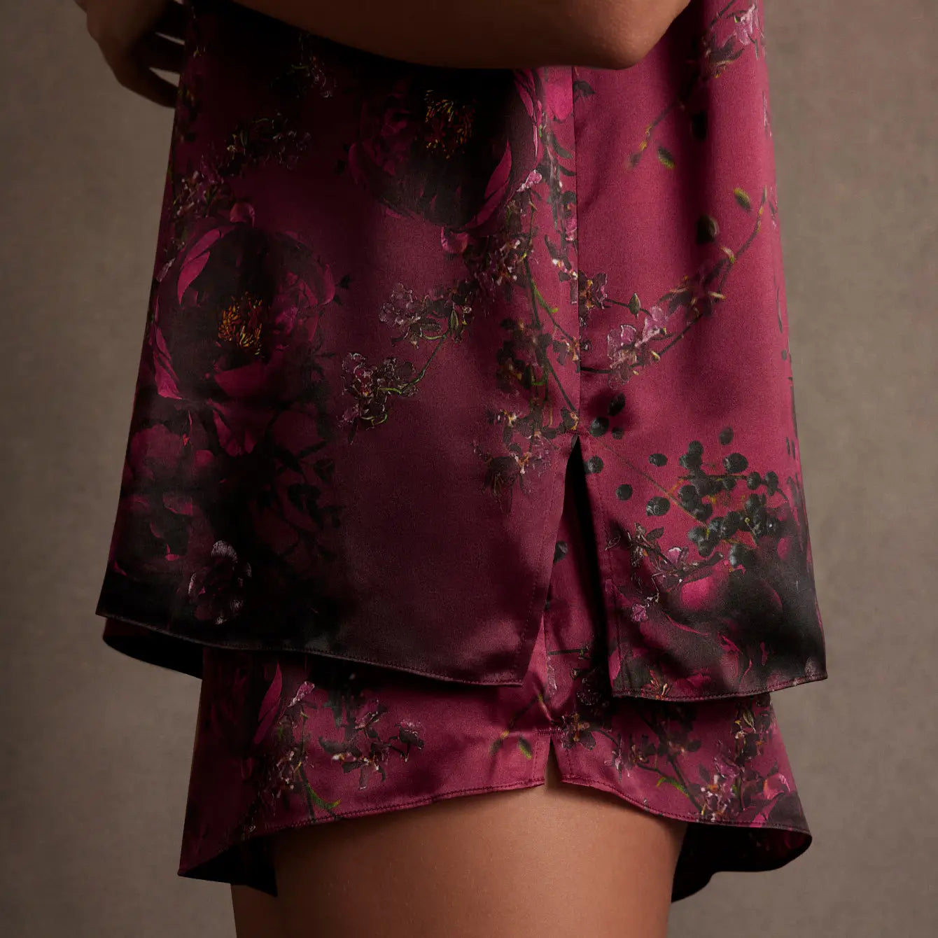 A close-up shows someone wearing Faire's Lunya Washable Silk Short and a dark floral satin top, both in rich burgundy and black. The matching set stands out against a neutral background.