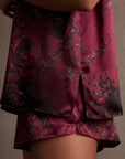 A close-up shows someone wearing Faire's Lunya Washable Silk Short and a dark floral satin top, both in rich burgundy and black. The matching set stands out against a neutral background.