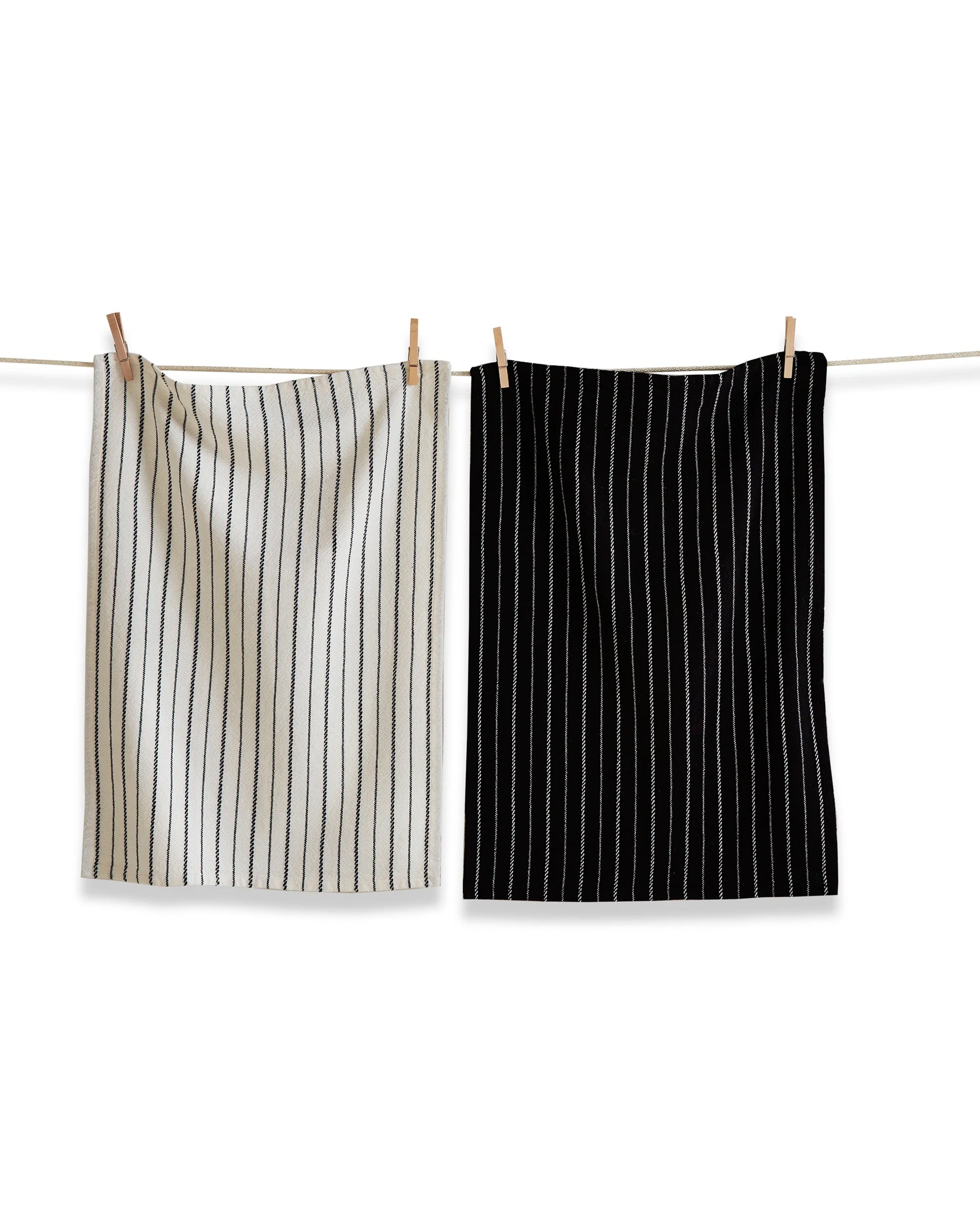 Two Tag Black Tie Stripe Towels hang on a clothesline with clothespins; featuring yarn dyed woven cotton for exceptional absorbency, one is white with black stripes and the other is black with white stripes.