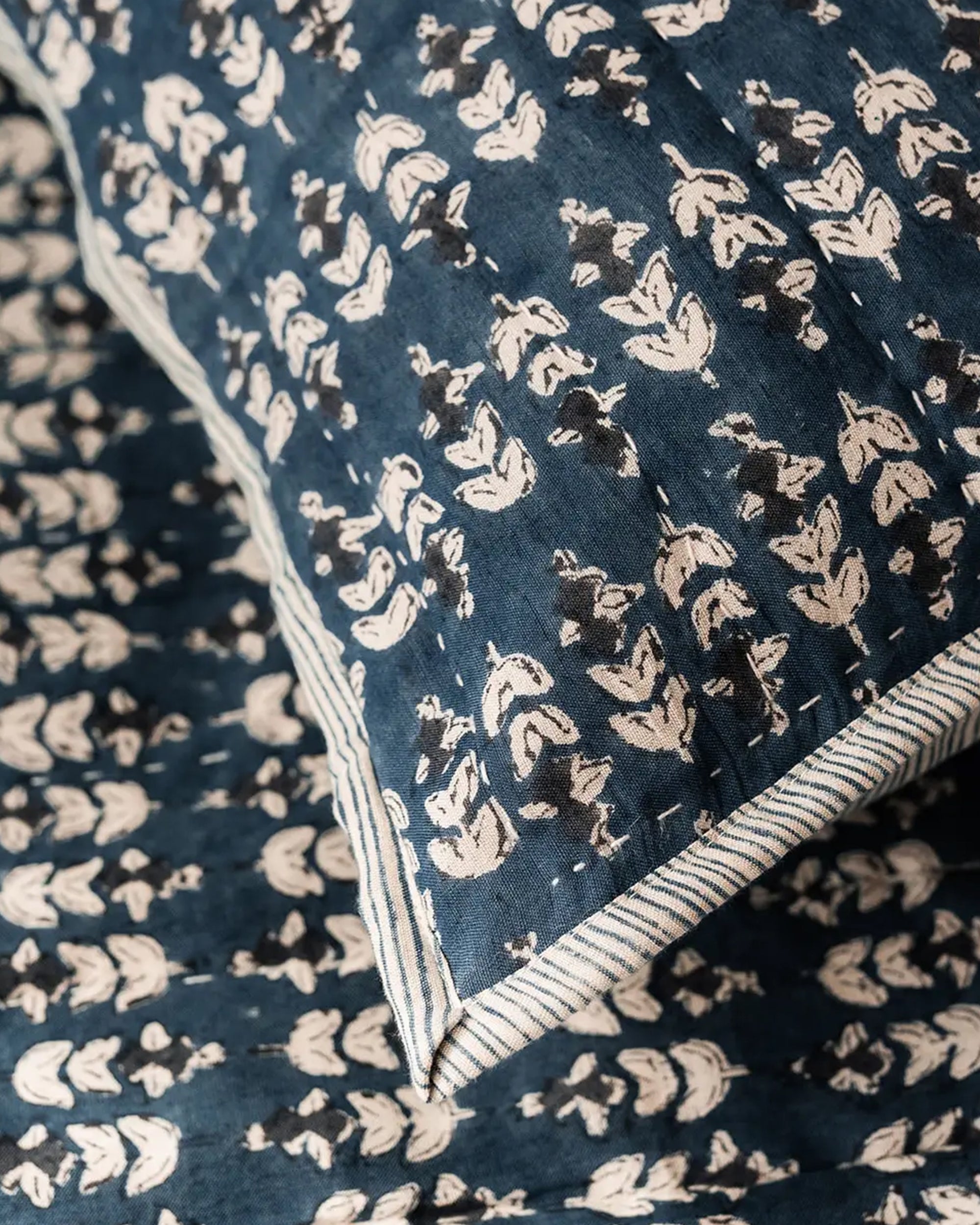 Close-up of the Faire Blossom Block Print Blanket, crafted in blue fabric with a white floral pattern and striped edging, featuring intricate hand-stitched details.