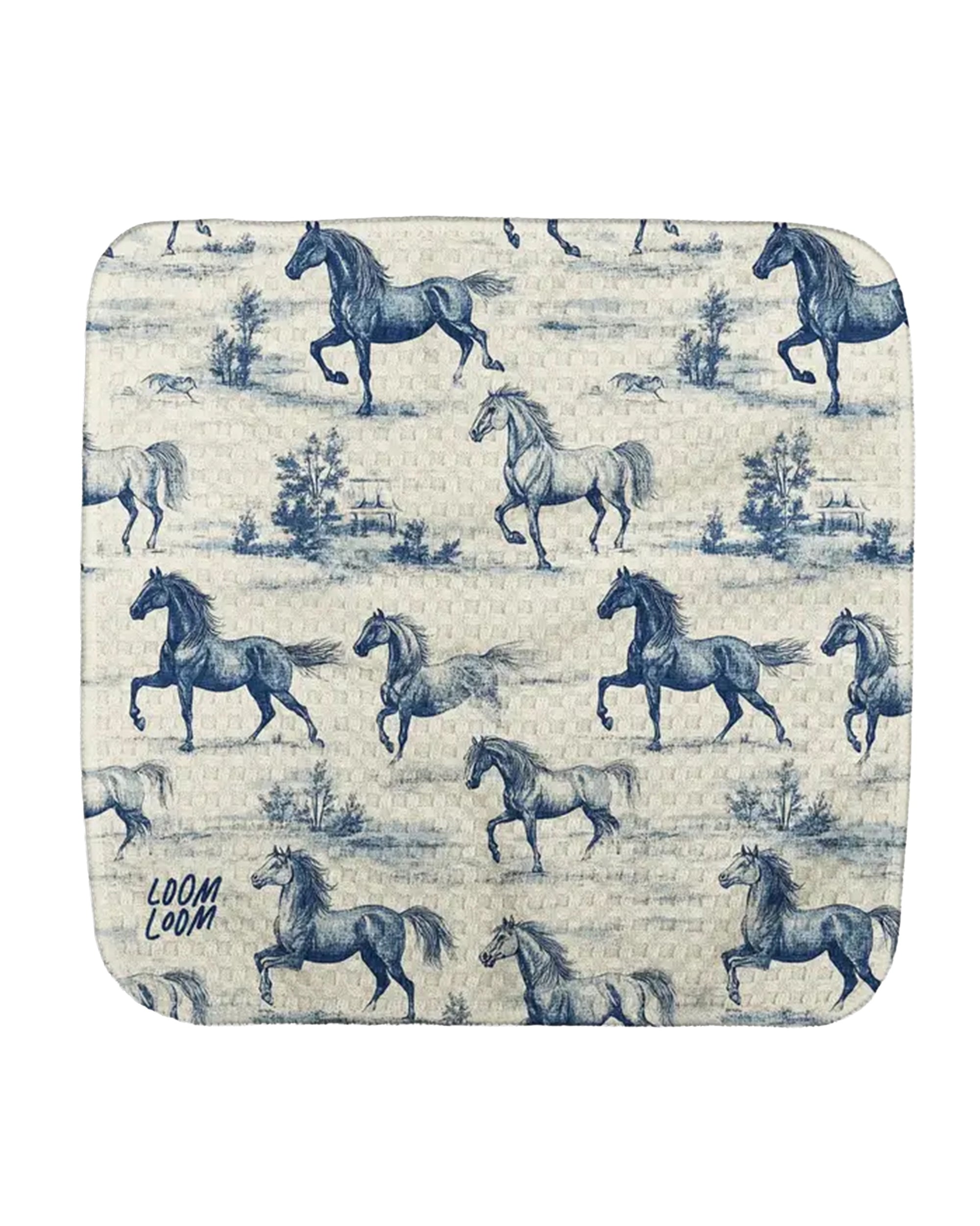 The Faire Blue Horses Dishcloth features a blue and white pattern with prancing horses and trees repeating across its surface. "LOOM LOOM" is printed in the lower left corner.