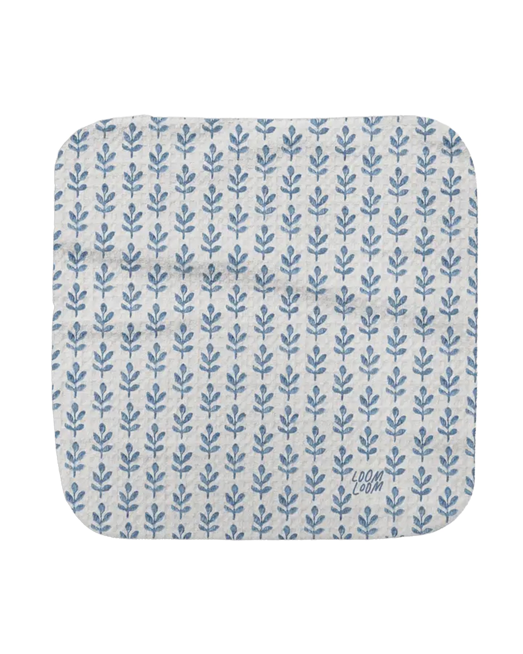 The Blue Stems Dishcloth by Faire is a white rectangular mat with rounded corners and rows of small blue leafy patterns, made from EcoLoom fabric. "LOOM LOM" appears in blue in the lower right corner.