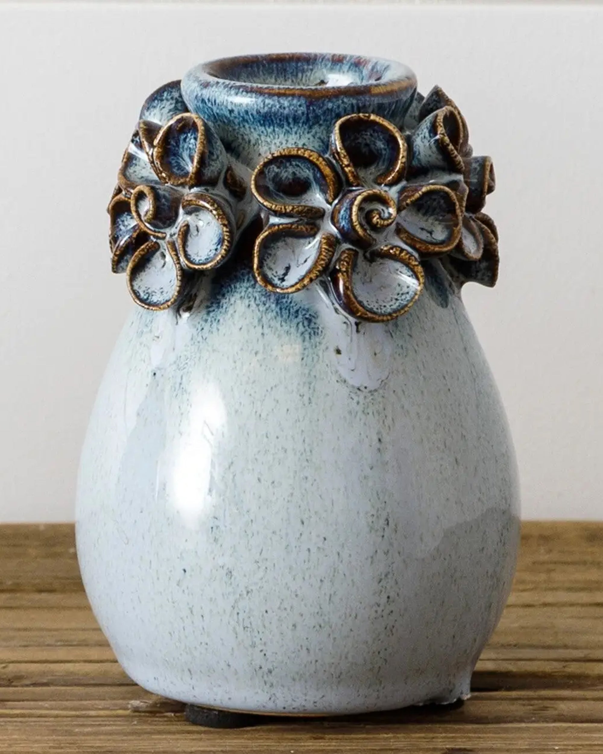 The Blue Bud Vase Sm by Faire is a small, handmade white ceramic vase with a glossy finish and raised, brown-edged floral designs near the opening—a charming decor piece for any home.