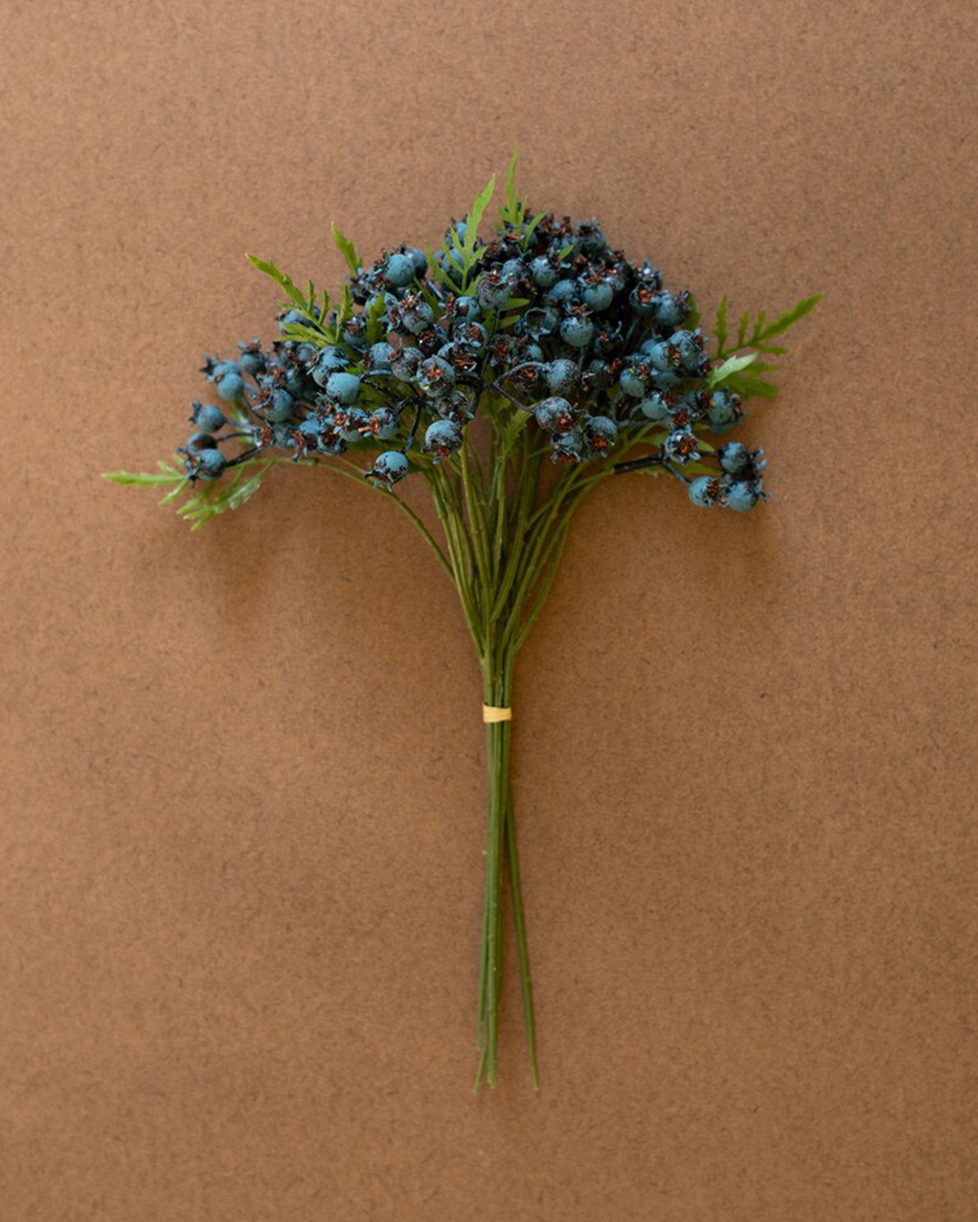 The CHAL1047 Blueberry Bundle by Kalalou, Inc features green stems with clusters of dark blue berries and fern-like leaves, all secured with a rubber band and displayed on a plain brown background.