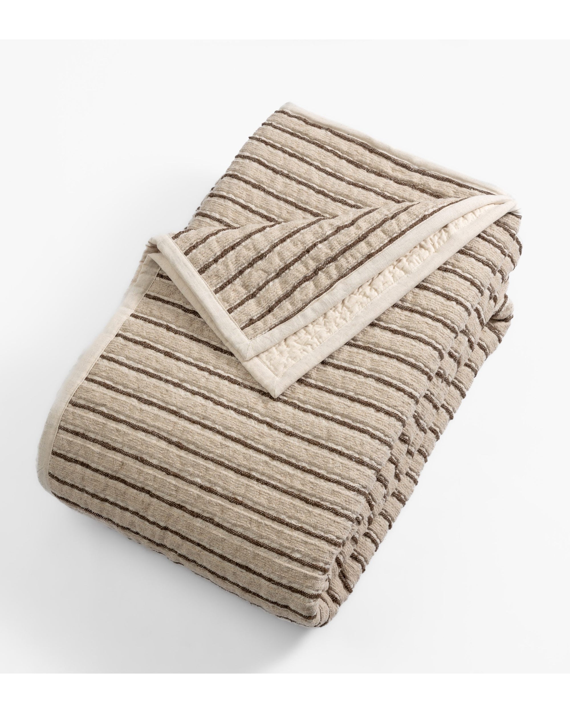 The Amity Home Bonita Quilt King features beige and brown stripes with a soft high-low texture. Displayed folded on a white background, one corner is turned to reveal its cozy linen-cotton underside.