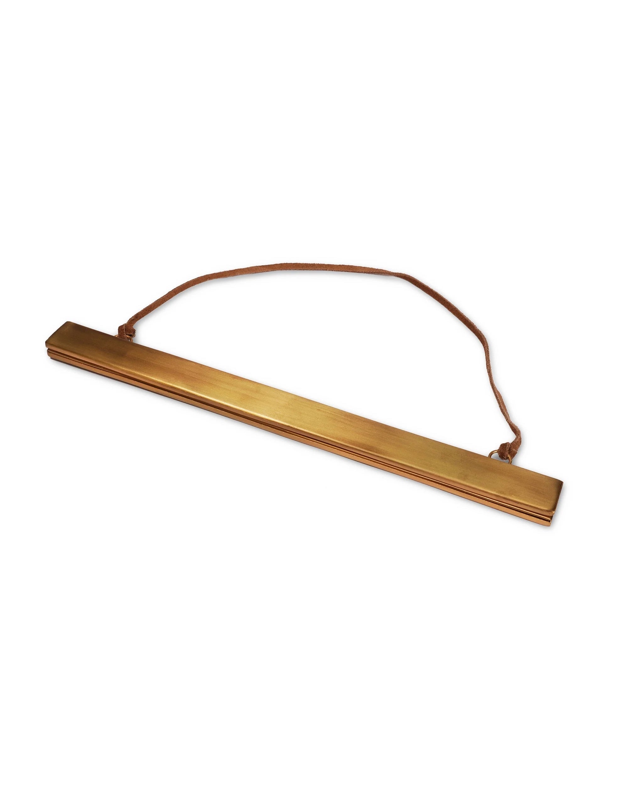 The Brass Magnetic Strip Frame by Sugarboo Designs is a long, rectangular brass frame with a brown leather strap at both ends, perfect for hanging your artwork or posters stylishly and easily.