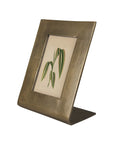 The Ridley Picture Frame by HomArt features a metallic easel design with a slanted base, shown displaying green and yellow leaf art on white, photographed against a plain white background.