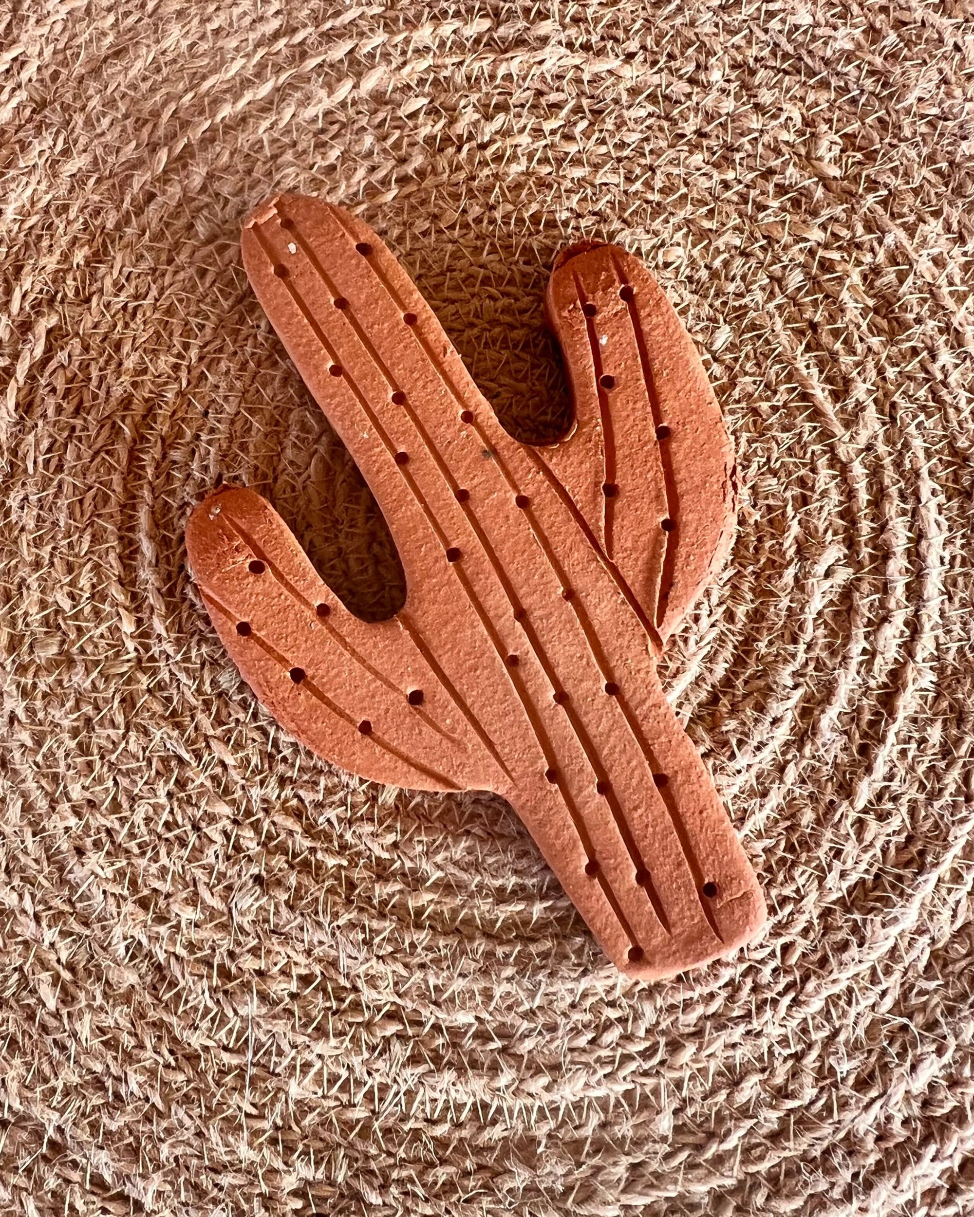 The Faire Brown Sugar Keeper is a handmade terra cotta ornament with carved lines and holes, shaped for function and style, resting on a circular woven straw mat.