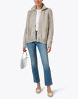 A person wearing the beige "Joy Sweater Coat" by Kerri Rosenthal with multicolor embroidery, paired with a white shirt, blue jeans, and beige shoes, holds a small silver handbag. They are standing in front of a white background.