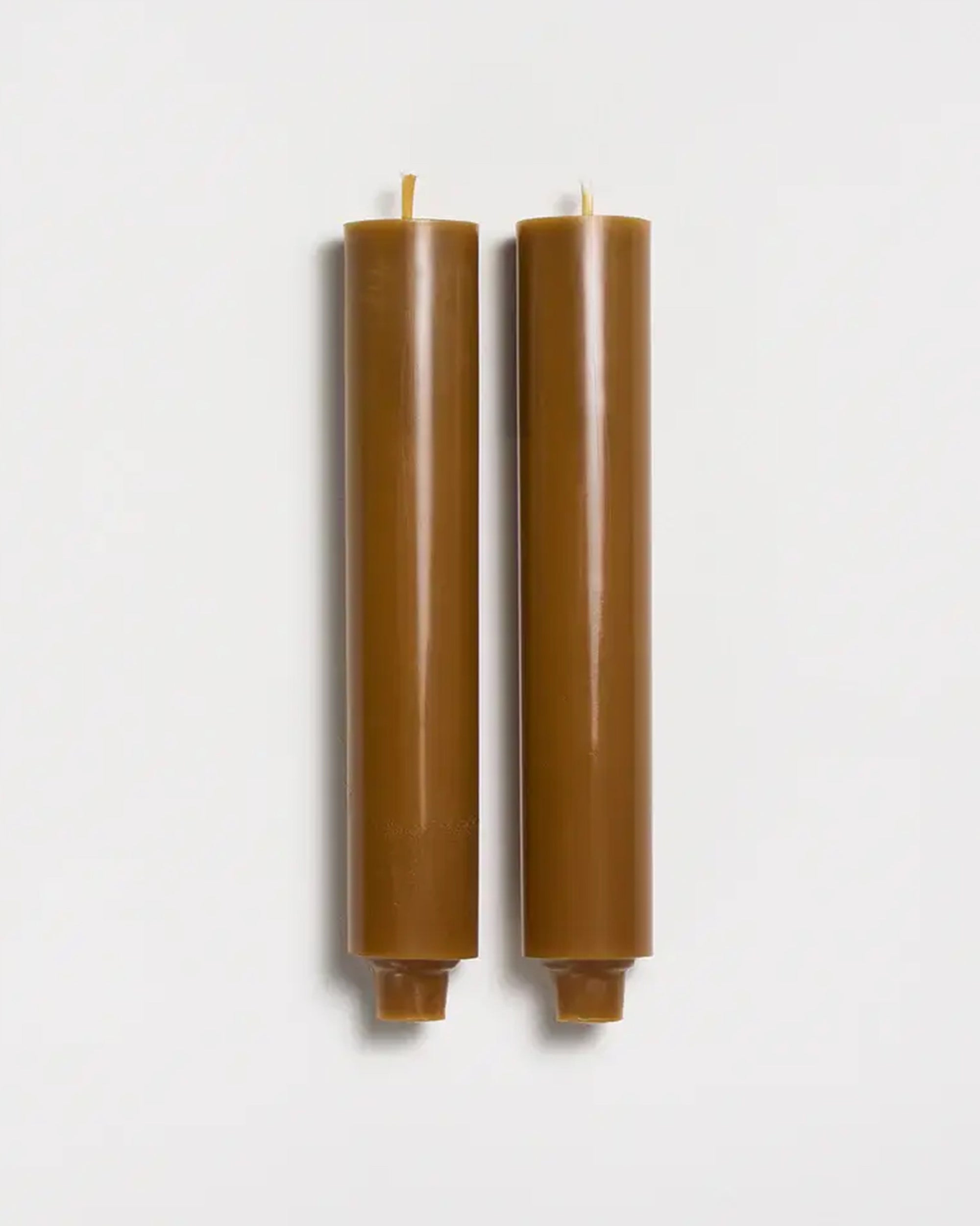 Two 9" Taper Candles in burnt orange by Faire stand upright side by side, featuring flat tops and bottoms, against a plain white background.