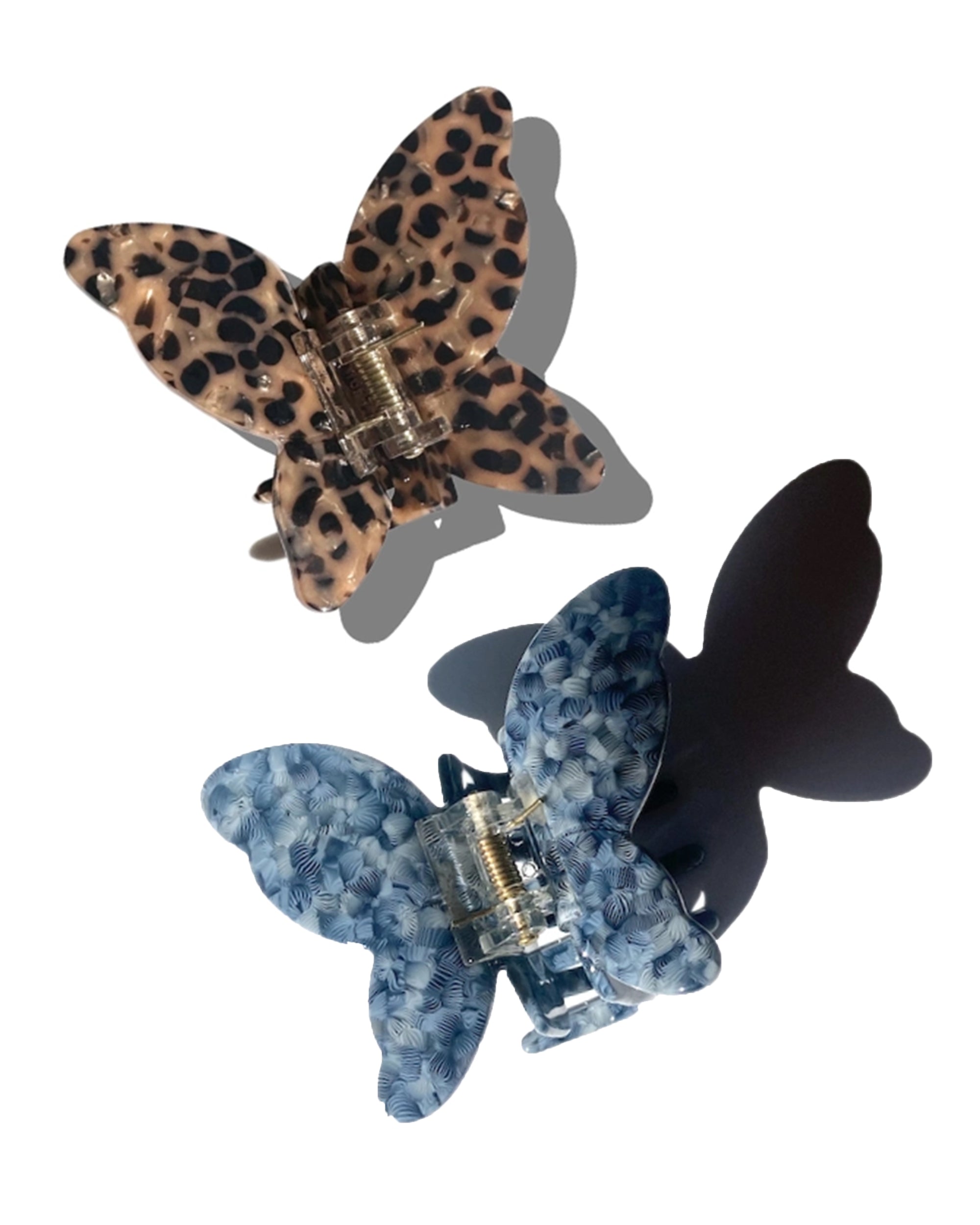 Two Fashion Hair Clips by Faire are displayed on a white background: one with brown and black leopard print, the other blue and white textured. Both are made from eco-friendly cellulose acetate with visible metal clasps casting soft shadows.