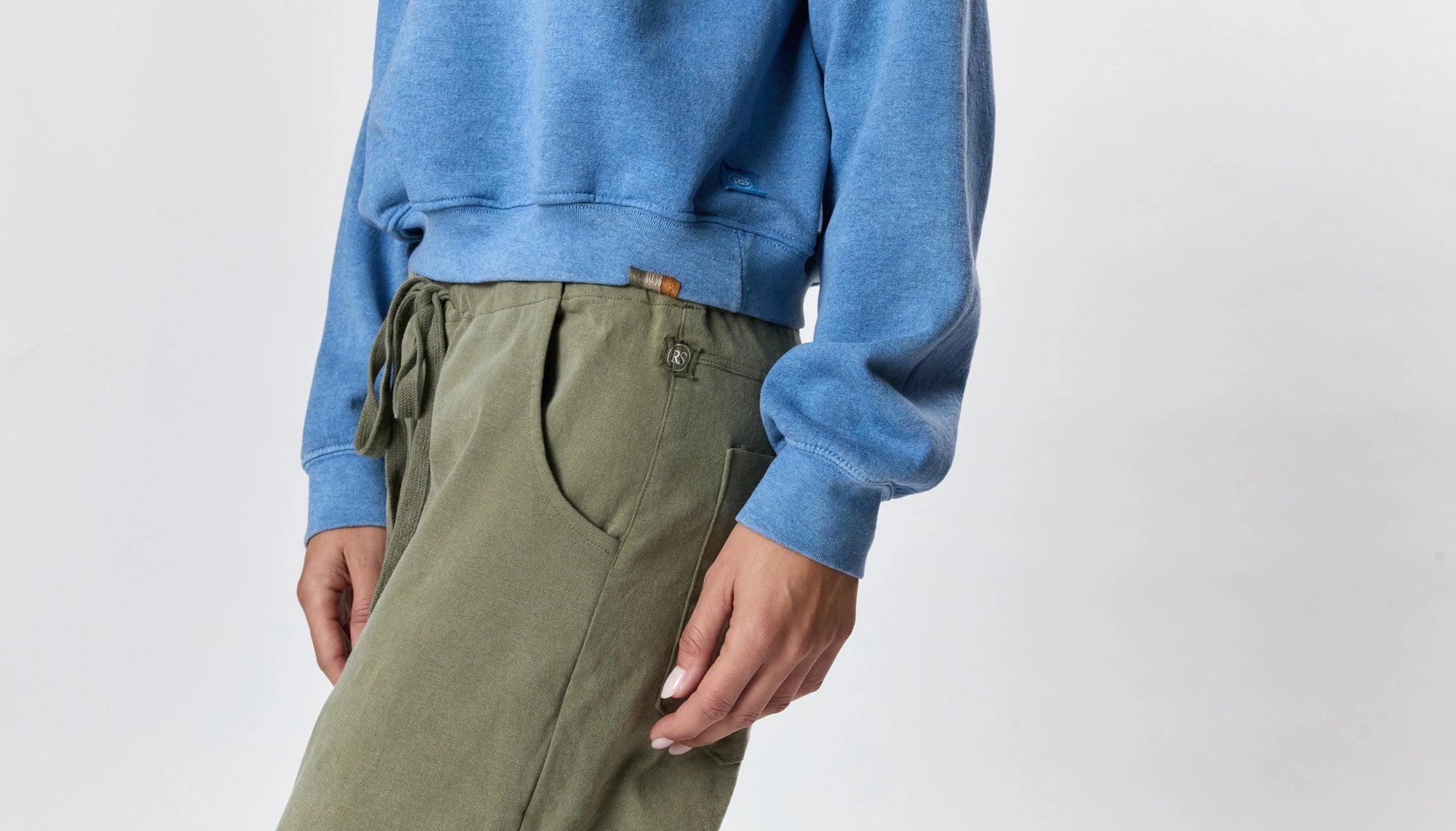 A person wearing Faire's Gwen Boyfriend Wide Leg Pant in organic cotton stands against a plain light background, with their left arm relaxed by their side and only the lower torso and upper legs visible.