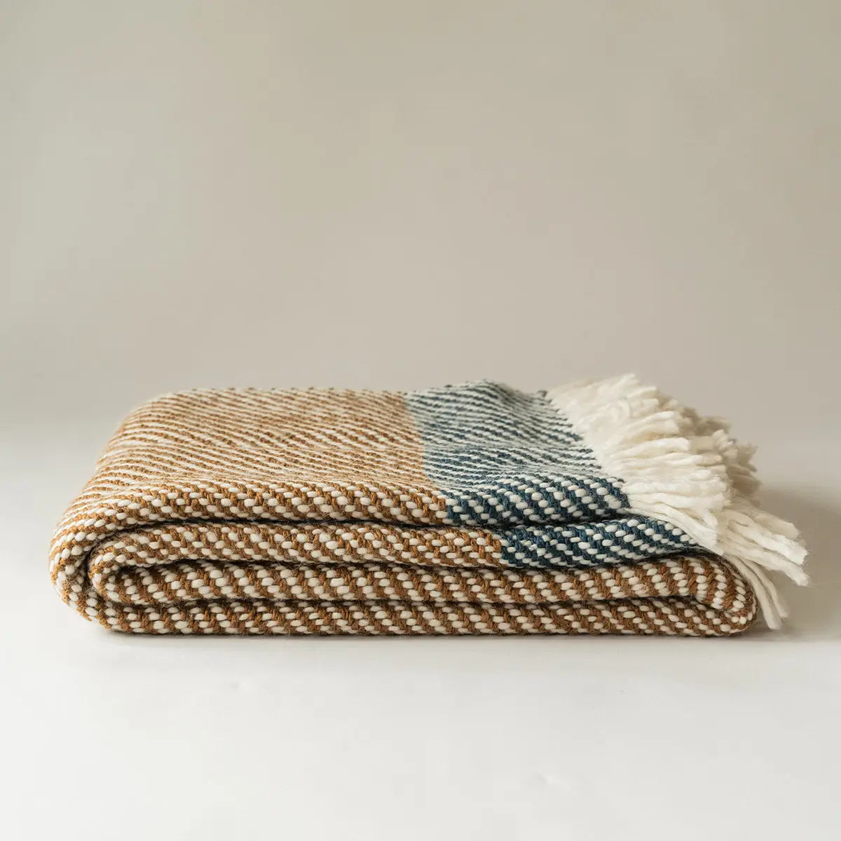 The Faire Chunky Twill Throw, featuring brown and cream patterns, dark blue checks, and white tassels on one end, is folded and displayed on a plain white surface.