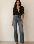 DOEN Henri top styled with high-waisted blue jeans and black heels, set against a simple light background.