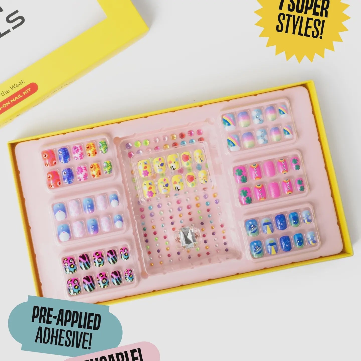 A vibrant yellow box of Faire's "Days of The Week Press on Nail Kit" features colorful nails with designs like rainbows, smiley faces, and leopard prints. The box boasts "7 Super Styles" and "Pre-Applied Adhesive.