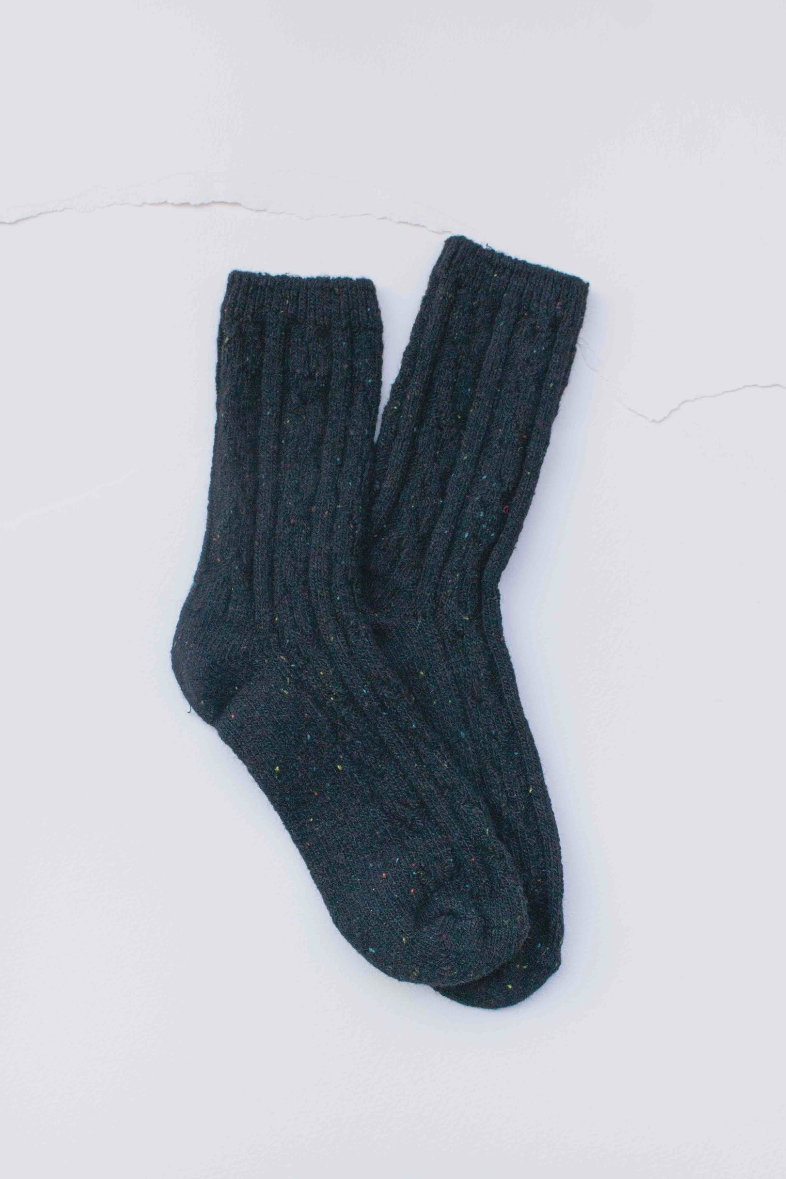 The Faire Wool Speckled Knit Socks, thick and dark-colored with a ribbed cable-knit pattern, are laid flat on a light surface.