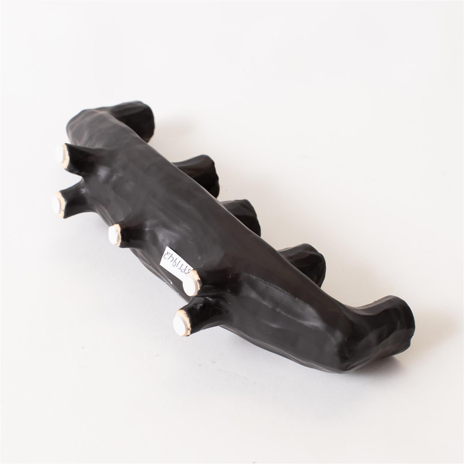 The Black Crescent Shape by Faire is a black, abstract ceramic sculpture with five rounded knobs, displayed on a white background. A small text label is attached to one side, making it a unique decor piece.