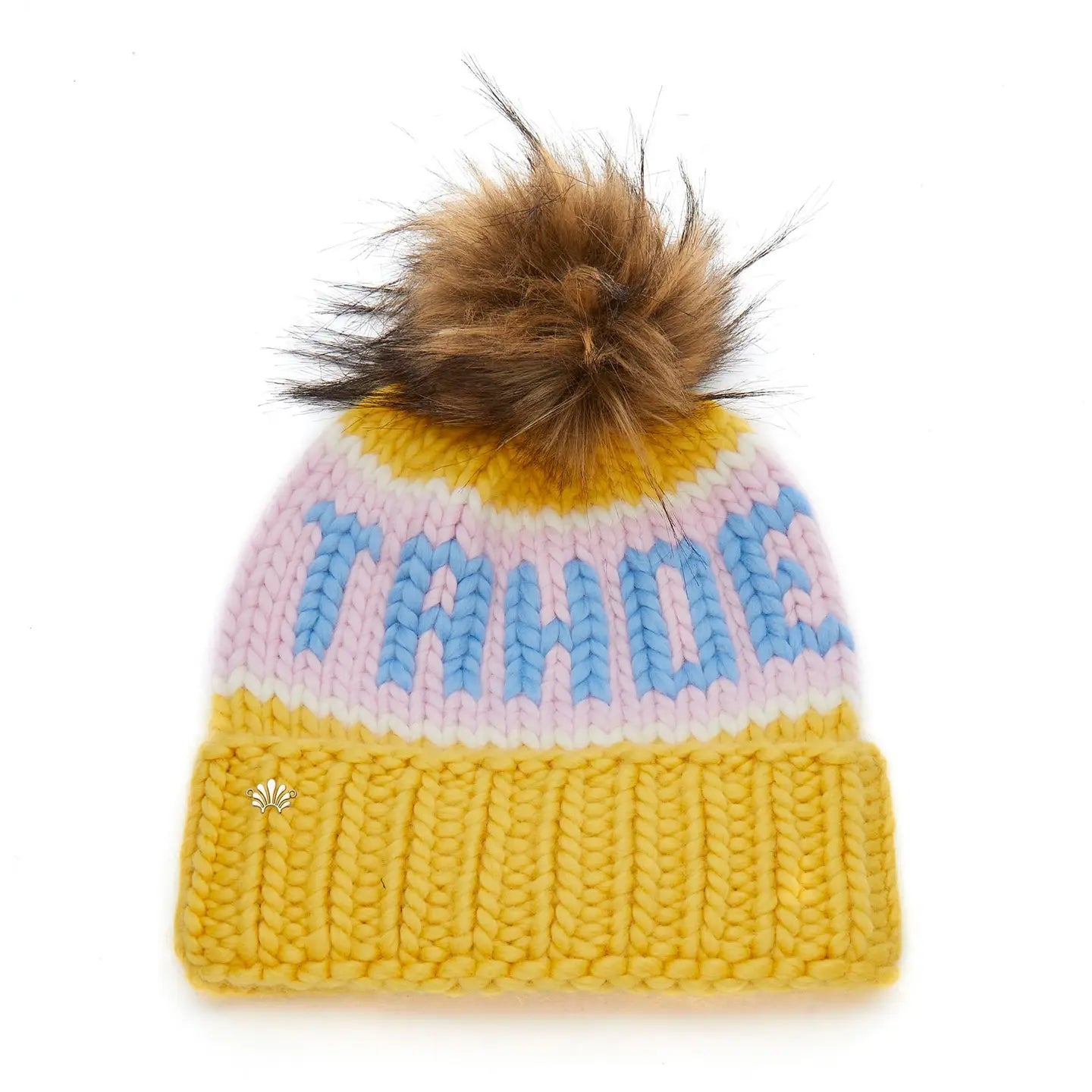 The Faire Knit Ski Hat is a luxury yellow merino wool beanie with pastel pink and blue stripes, “TAHOE” in blue letters, a folded brim, and a large brown faux fur pom pom on top.