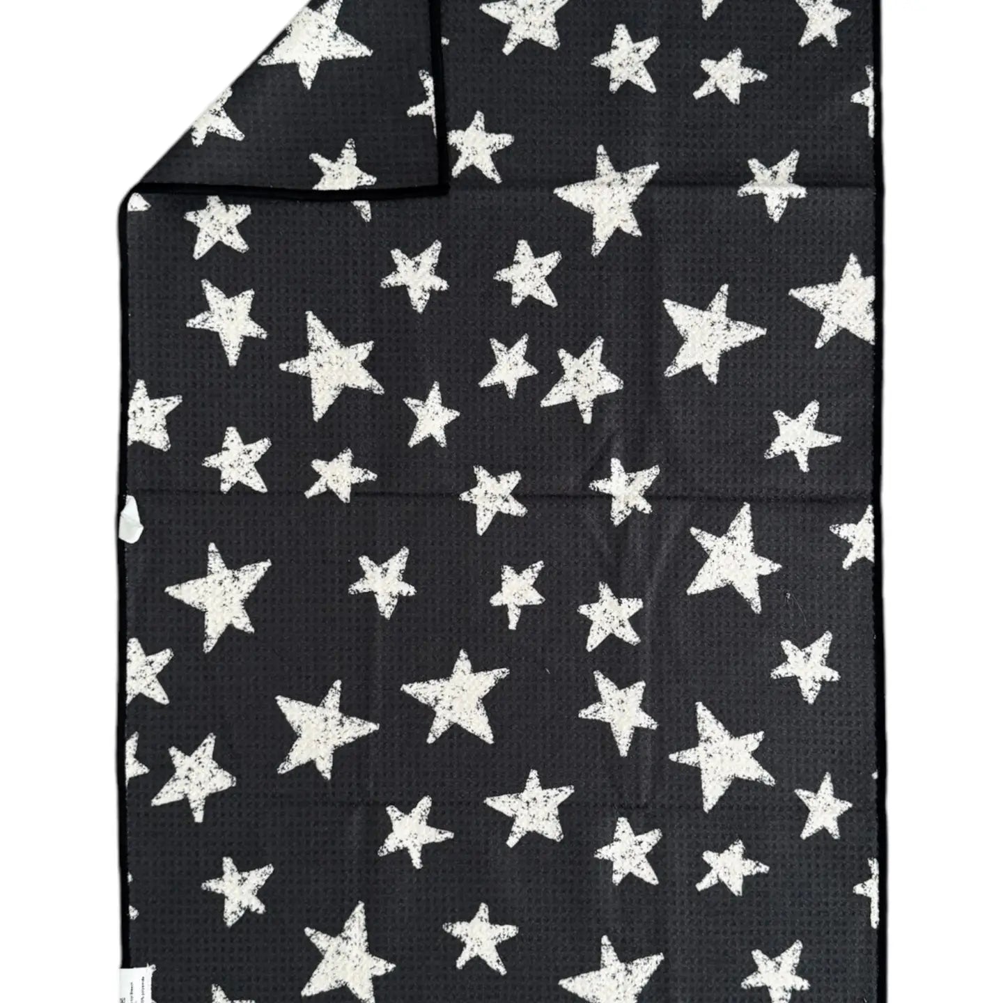 The Faire "Hand Towel : Into The Stars" is a black rectangular waffle weave microfiber towel with white stars of various sizes. A folded corner shows that the same star pattern appears on both sides.