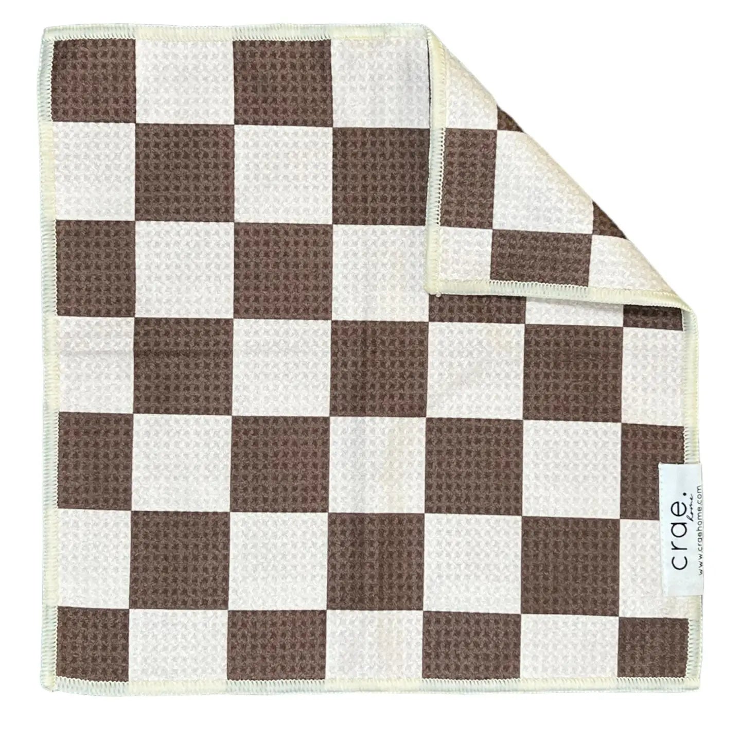 A brown and white checkerboard waffle weave microfiber washcloth with a textured, high-absorbent surface is shown. One corner is folded to reveal the reverse side and a white tag with the brand name "Faire" is visible.