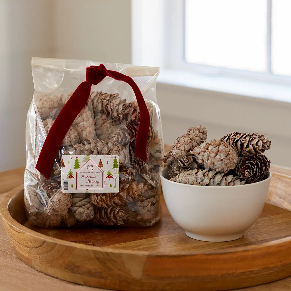 Faire's Christmas Potpourri White Cones come in a clear bag with a red ribbon and holiday label, offering frosted pine cones that bring an earthy fragrance to your festive decor.