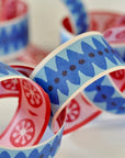 Faire's Paperchain features colorful, biodegradable decorative links with blue, red, and pink geometric and floral patterns, arranged loosely overlapping on a light surface.