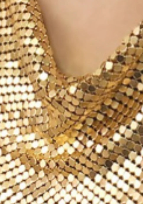 A close-up of shimmering gold sequin fabric in folds, showcasing Faire's Chain Mail Bandana Scarf Necklace at the neckline.
