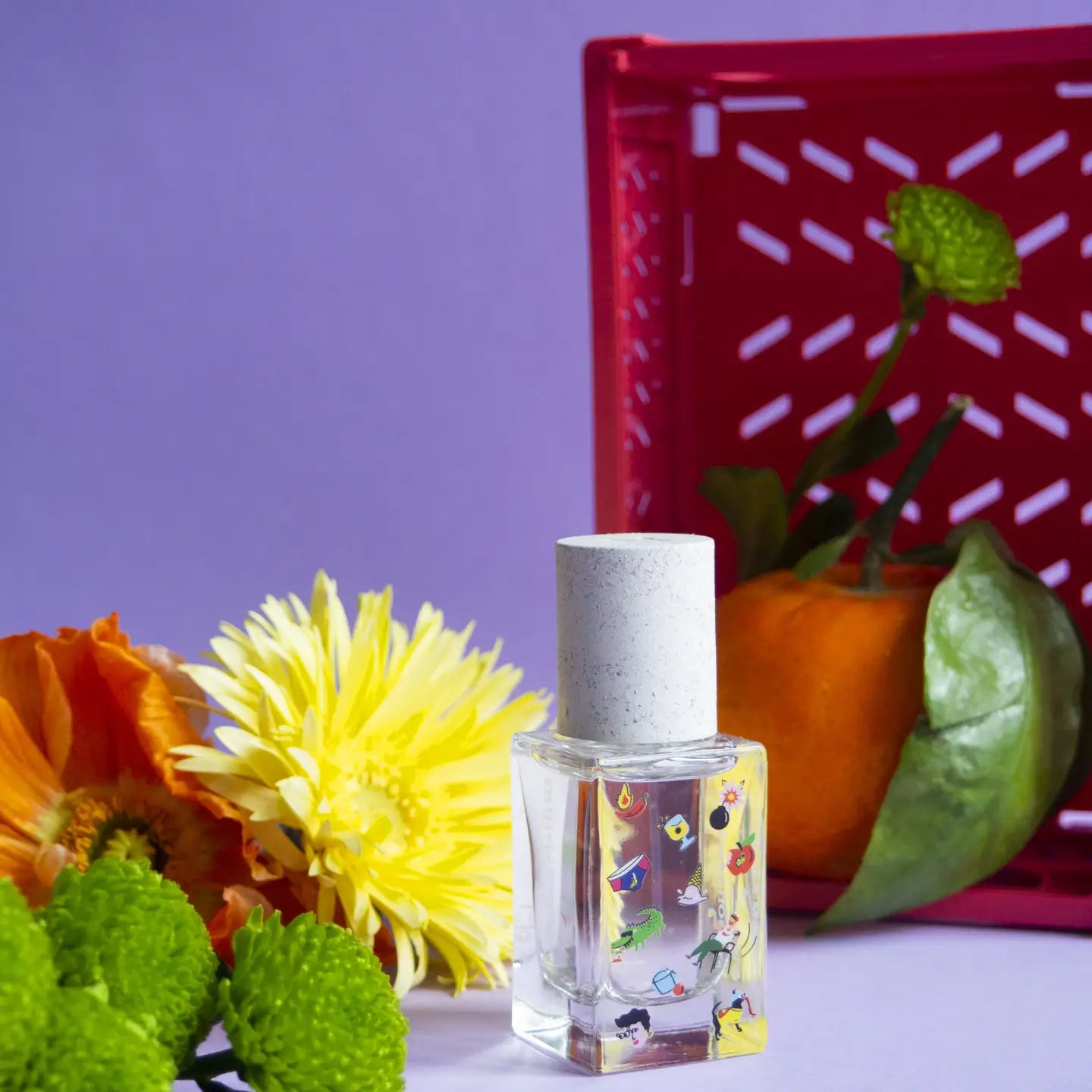 Maison Matine Perfume by Faire—a clear bottle with a white cap and colorful cartoon designs—rests on a purple surface with orange and yellow flowers, green chrysanthemum buds, tangerine, and hints of vanilla against a purple background.