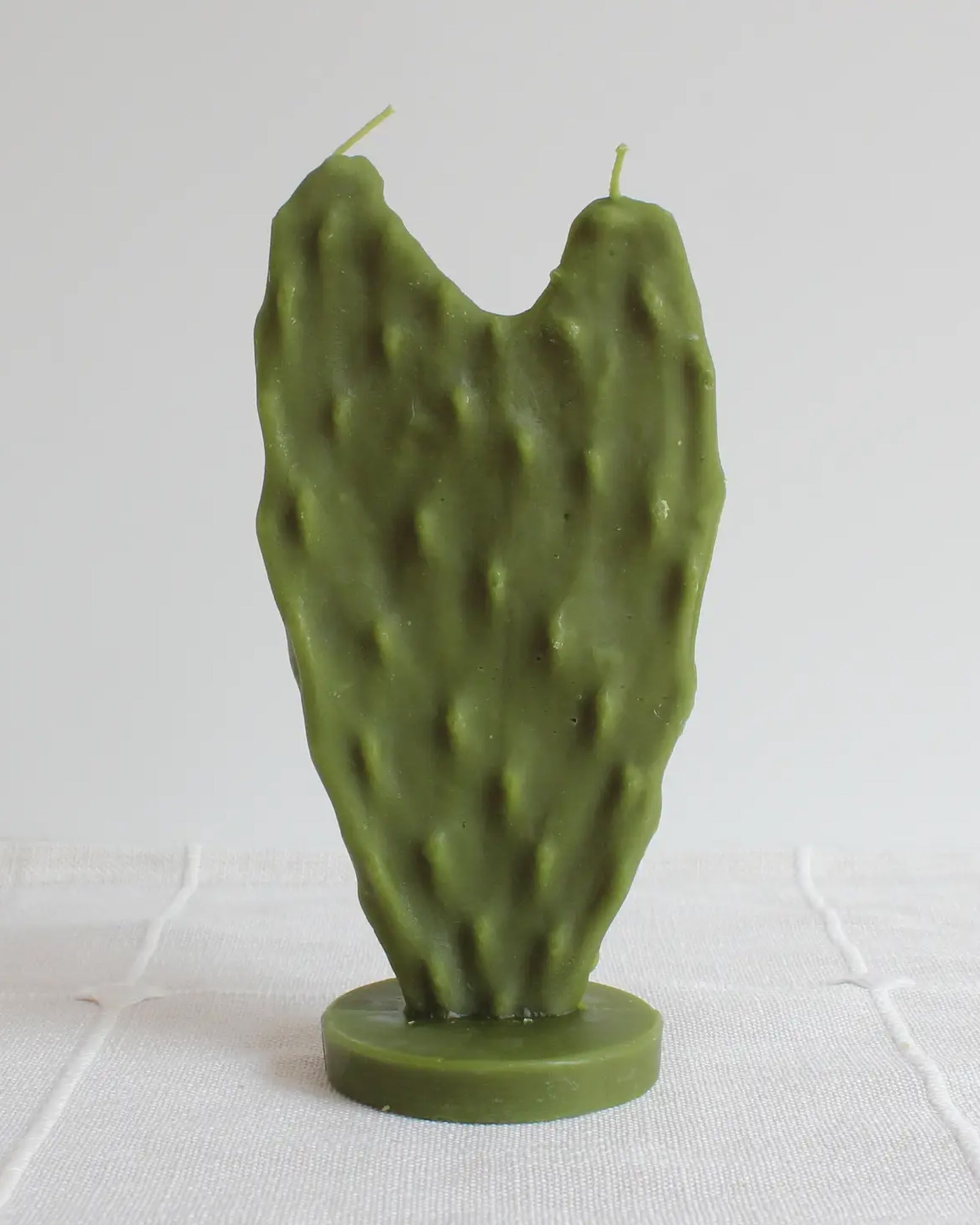 The Faire Nopal Cactus Beeswax Candle features two wicks and stands upright on a circular base, beautifully shaped like a cactus paddle—an eye-catching piece of home décor shown against a plain white background.