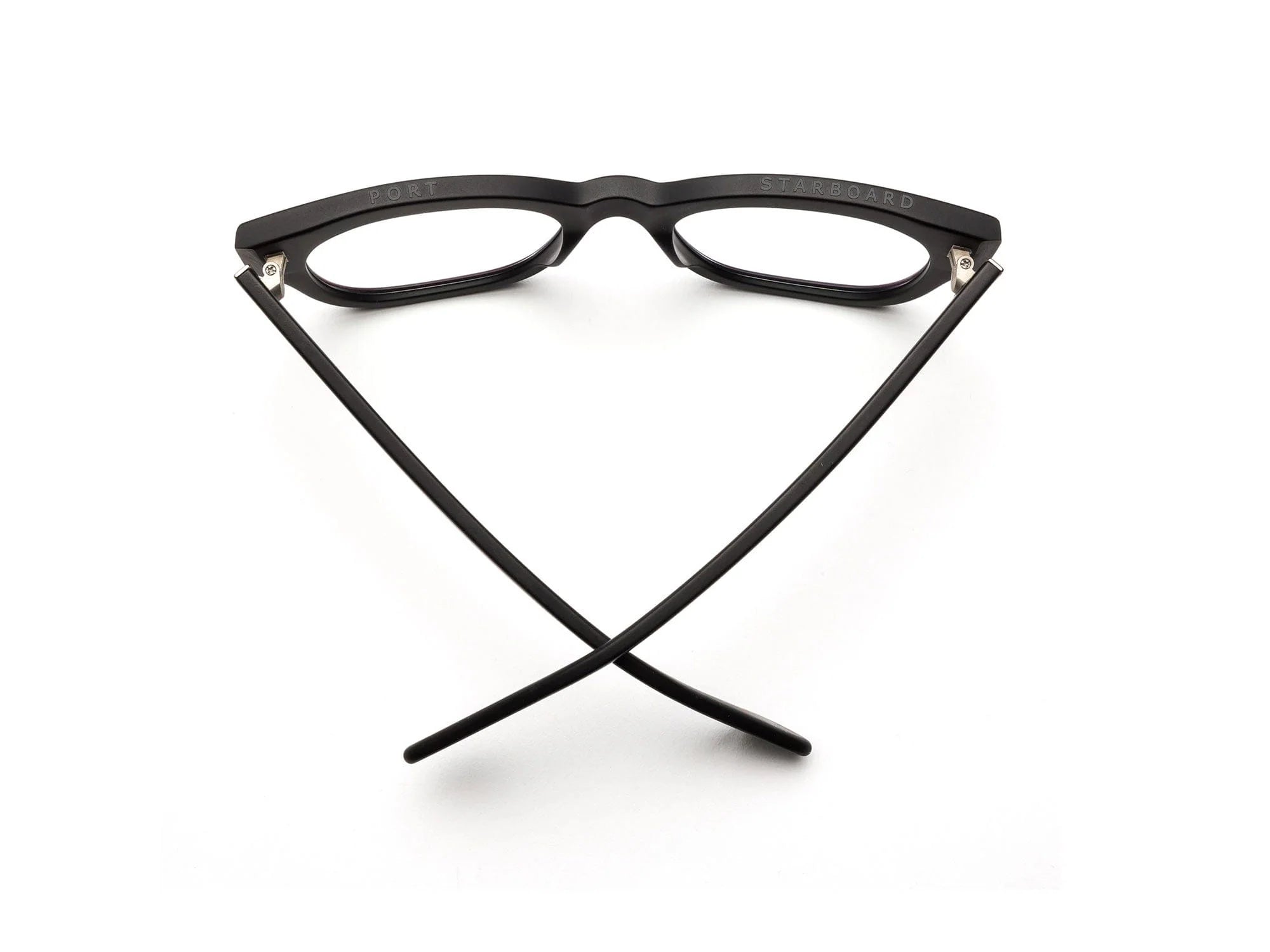 A pair of Caddis Miklos Matte Black eyeglasses is placed upside down on a white surface, with the arms open and crossed in a V shape.