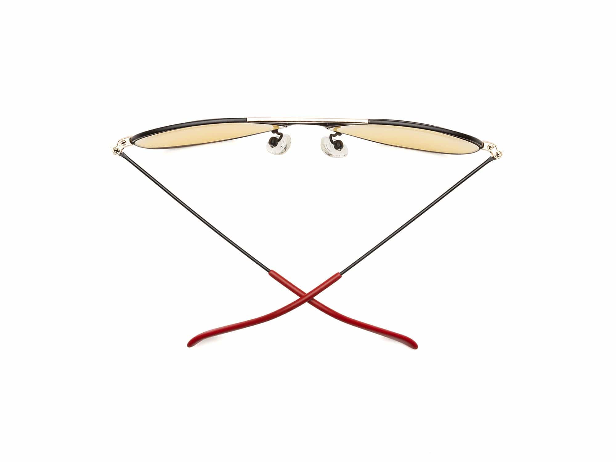 Caddis Mabuhay Matte Black sunglasses feature yellow tinted lenses and thin wire aviator arms, shown from the back with red rubber temple tips crossed at the bottom against a white background.