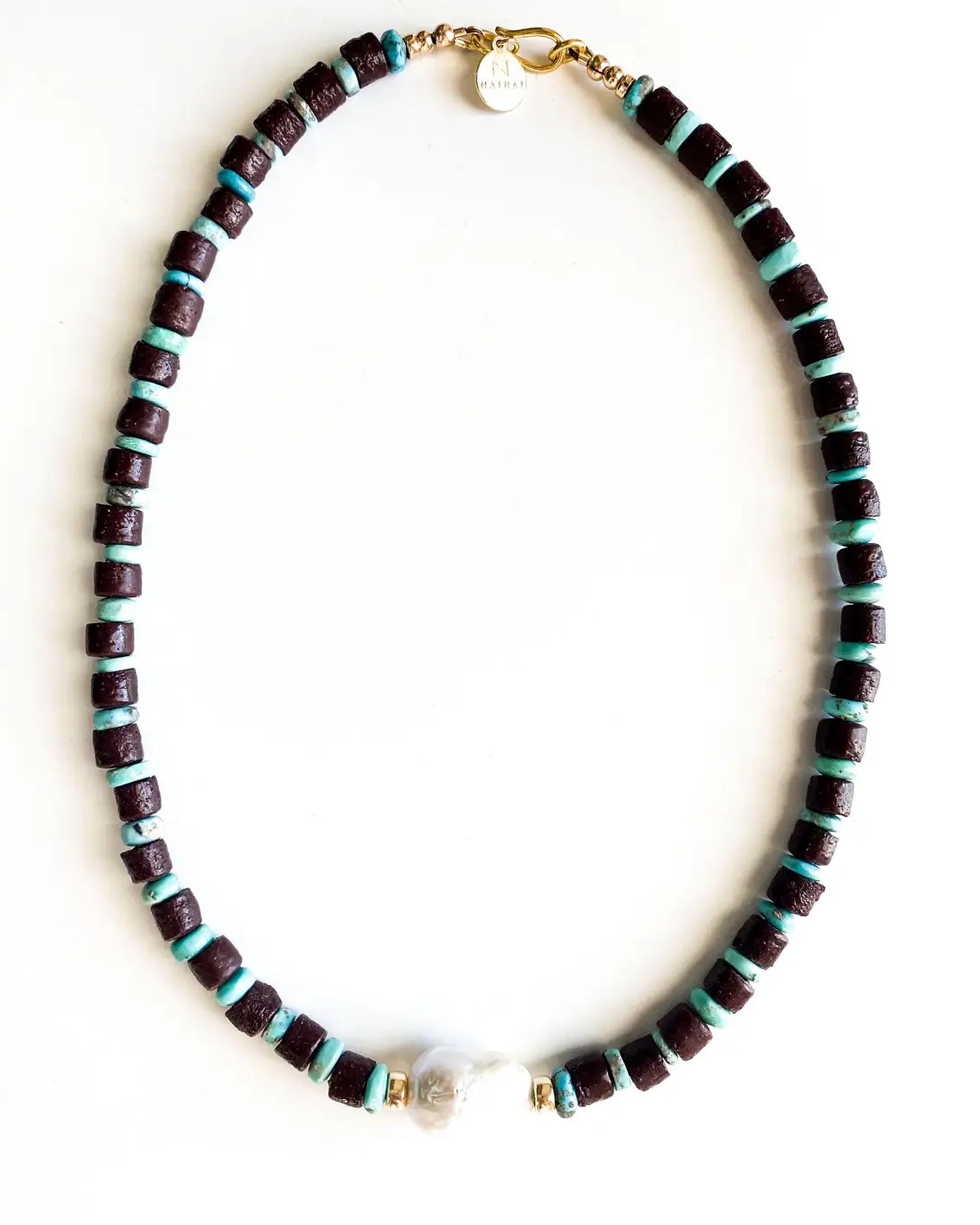 The Faire Cadeau Necklace features alternating dark purple and turquoise African glass beads, highlighted by a unique freshwater baroque pearl near the clasp, shown against a white background.