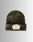 The Faire Patch Beanie Support Your Local Mother features a camo knit, folded brim, and a white-orange patch with "SUPPORT YOUR LOCAL MOTHER. EST 2023." Displayed on a light gradient background.