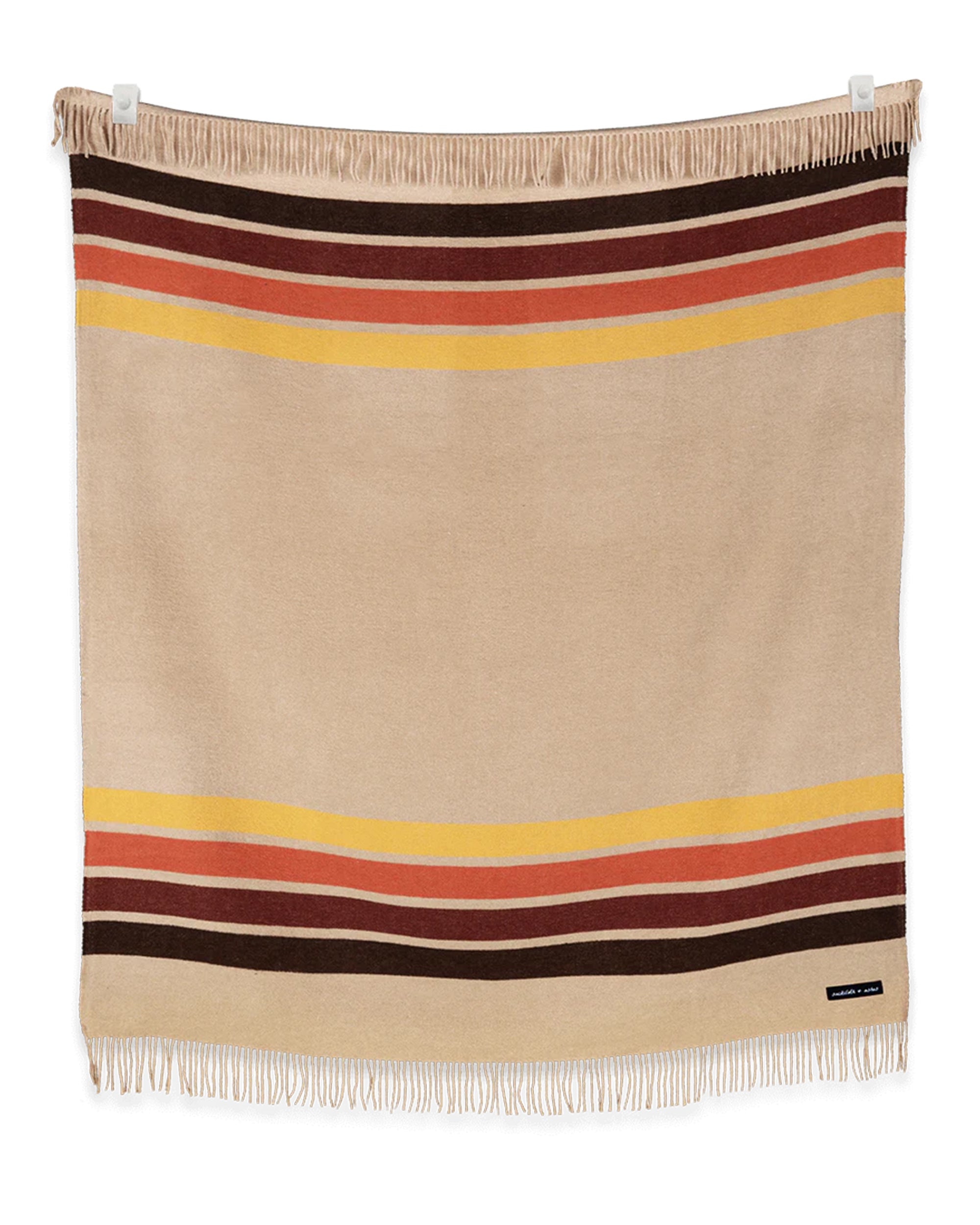 The Sackcloth & Ashes/Desert Camp blanket by Sackcloth & Ashes showcases beige fabric with red, brown, and yellow stripes near the edges, finished with fringe on both ends and displayed flat against a white background.