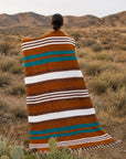 Faire Canyon Cove Handwoven Blanket by Bungalow draped on person in a desert landscape with mountains and shrubs.