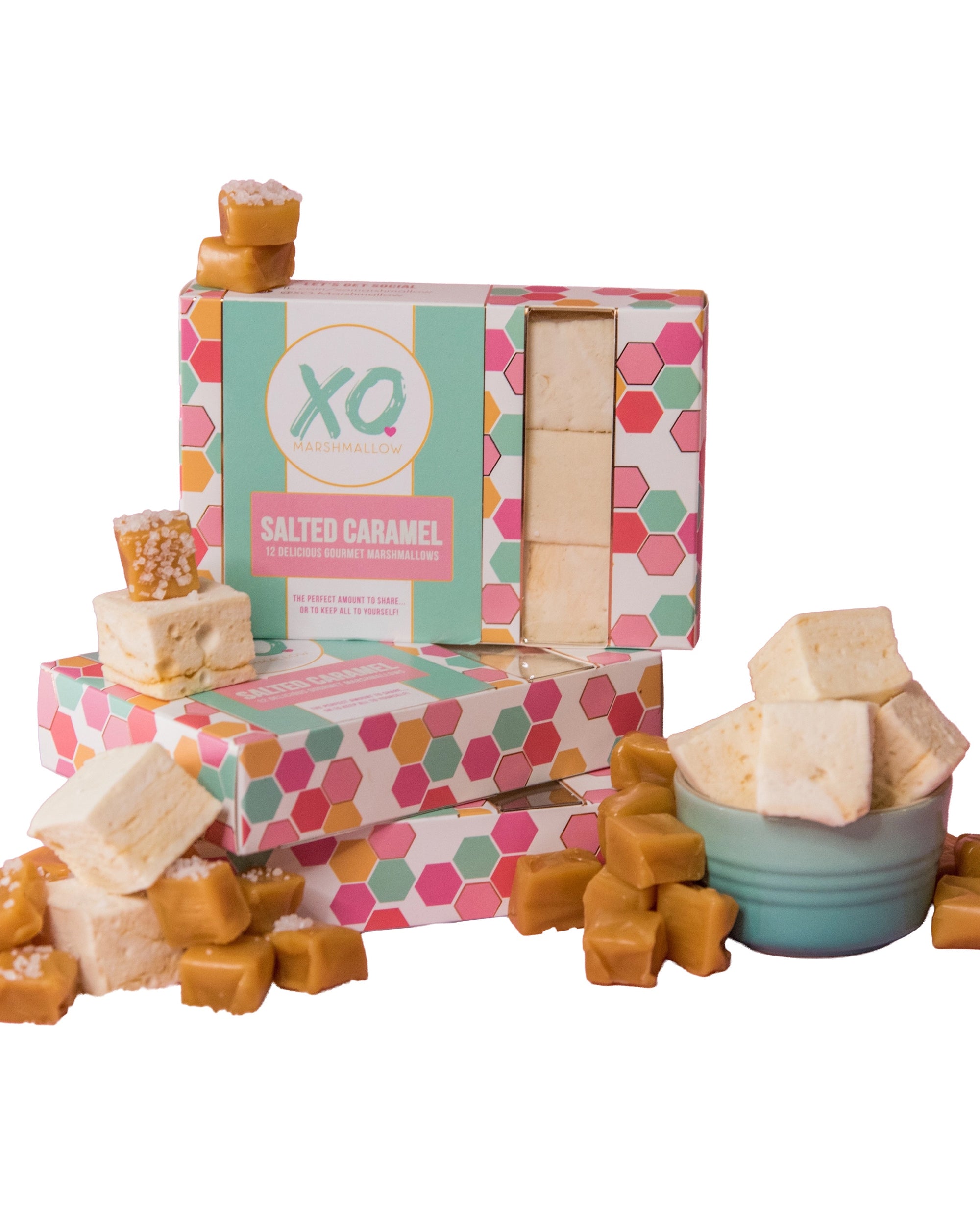Boxes of Faire Salted Caramel Marshmallows are stacked, surrounded by allergy-friendly marshmallows and caramel candies, with a bowl of fluffy salted caramel cubes placed in front.