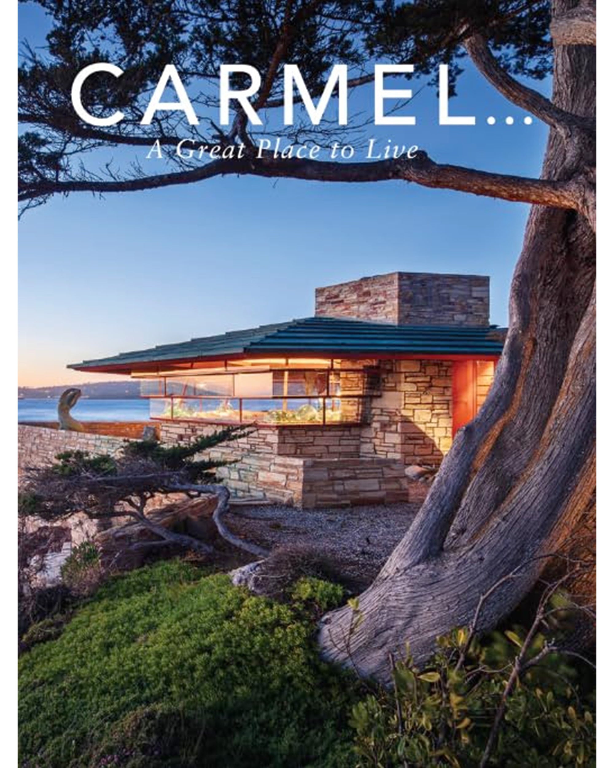 A modern stone and glass house by the ocean along California’s coast, surrounded by trees at sunset. Text reads: “Carmel by Rhino Publishing—A Great Place to Live.”.