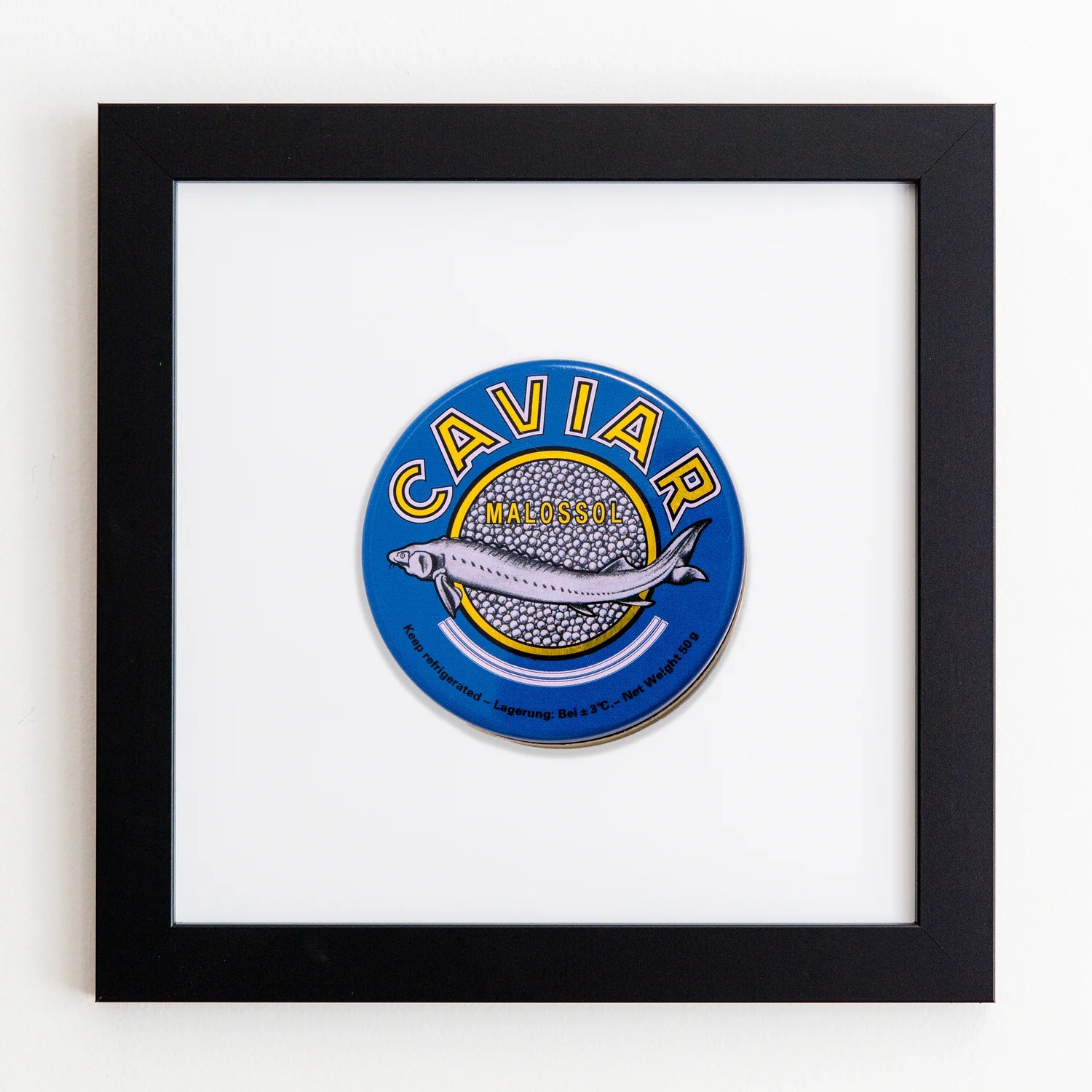 A framed acrylic image featuring a vibrant circular label for &quot;Malossol Caviar,&quot; with a stylized silver fish surrounded by a blue and yellow color scheme, in an Art Square Black Frame by Match South.