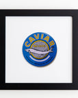 A framed acrylic image featuring a vibrant circular label for "Malossol Caviar," with a stylized silver fish surrounded by a blue and yellow color scheme, in an Art Square Black Frame by Match South.